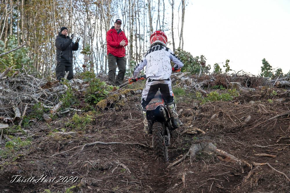 dirt biker climbing a hill with two people encouraging him