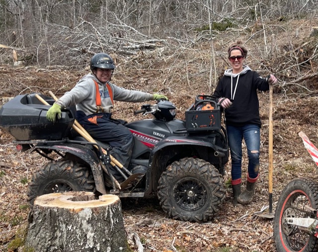 Man on ATV and woman with rake in front on a trail