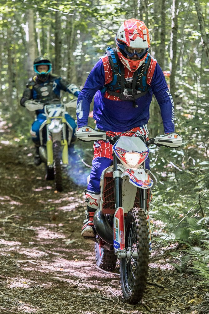 two dirt bike riders riding in the woods 