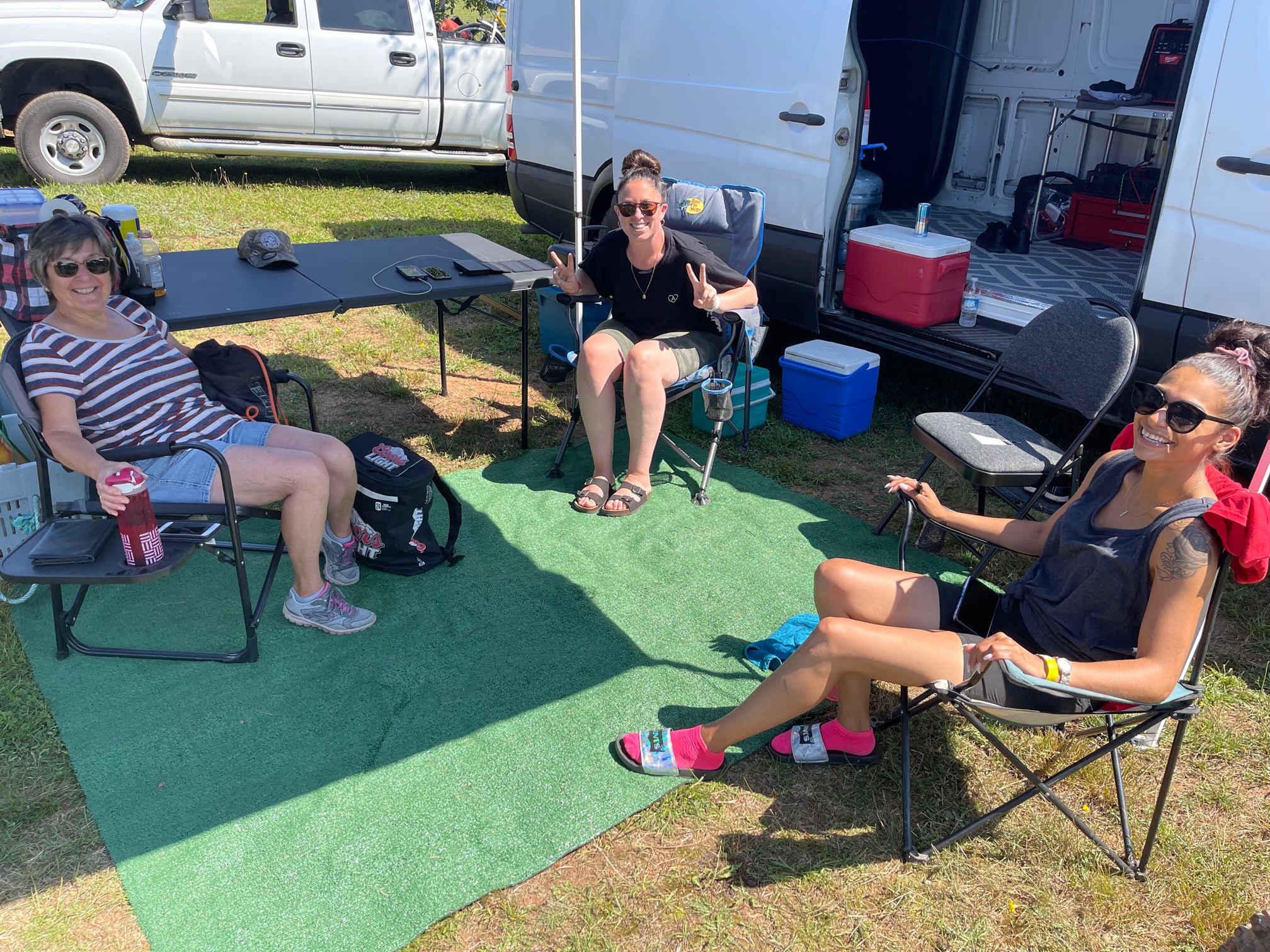 Three women under a tent next to a camper trailer