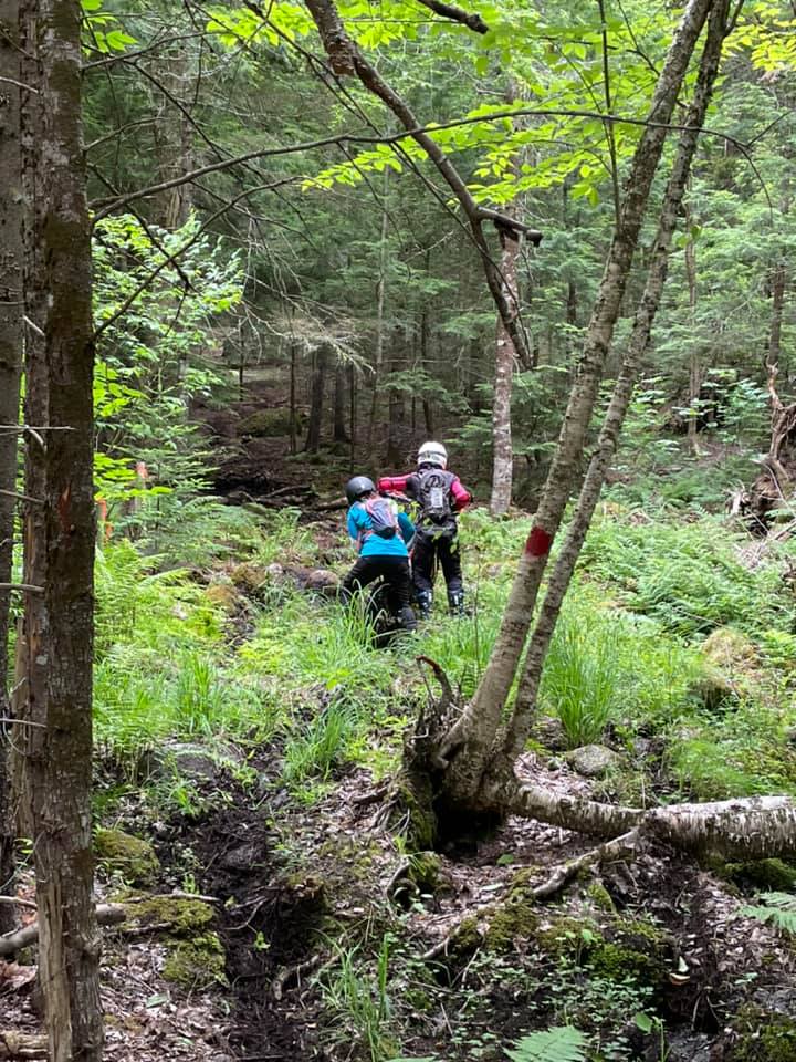 Two riders going through rough woods terrain