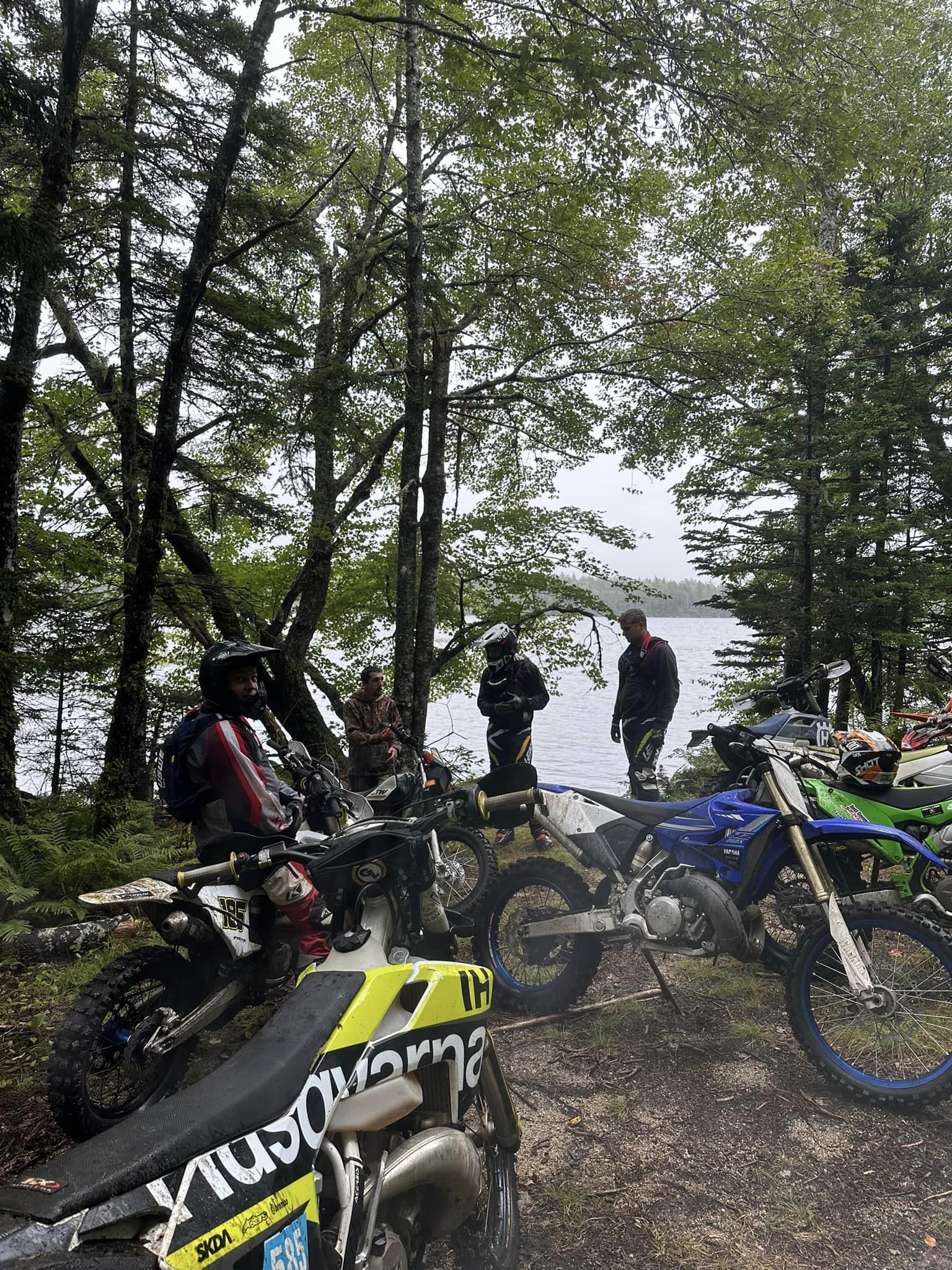 riders with their bikes in the woods with water in the distance